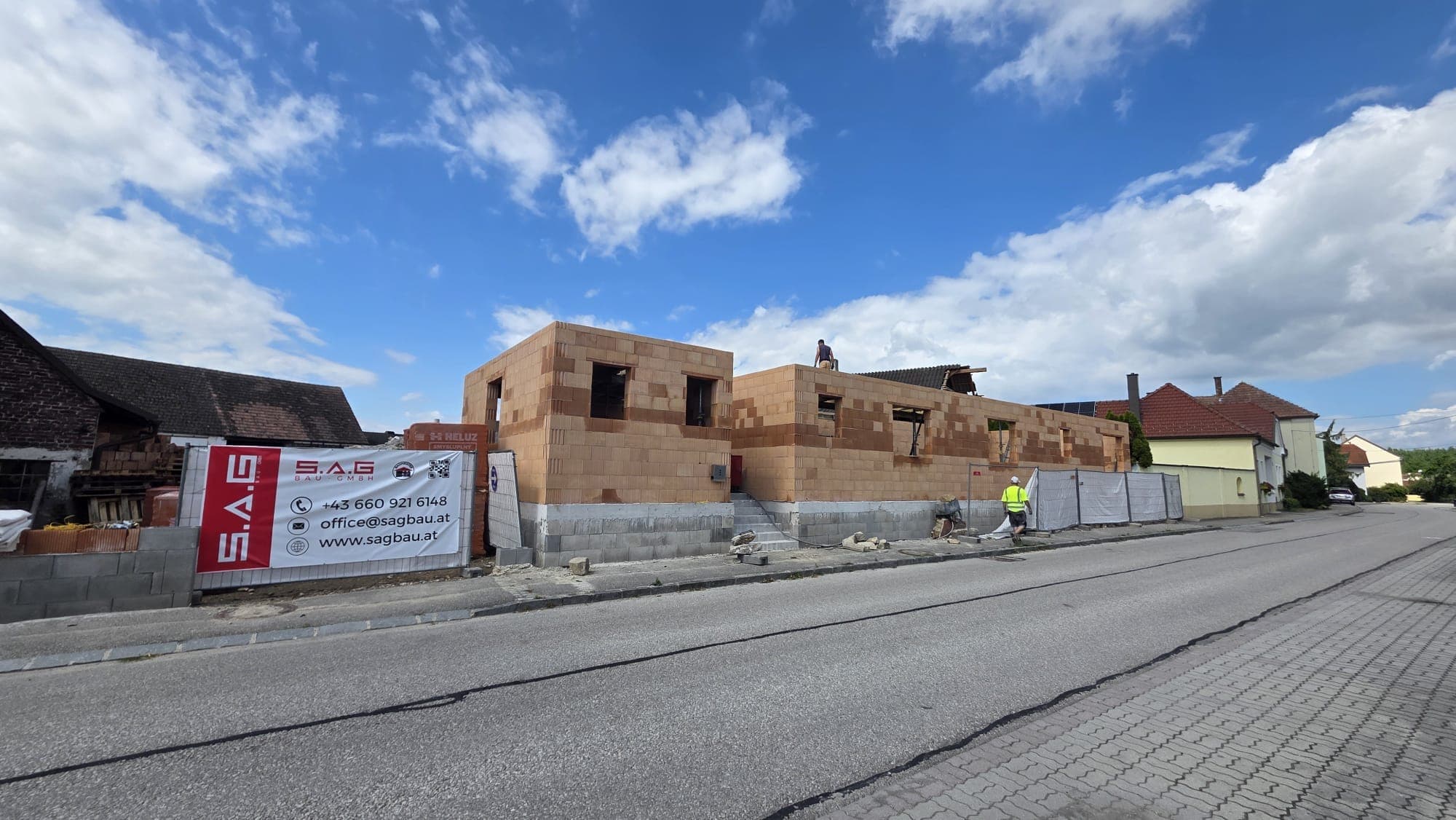 Ziegelrohbau an der Straße mit SAG-Bau-Banner am Bauzaun, Langenschönbichl